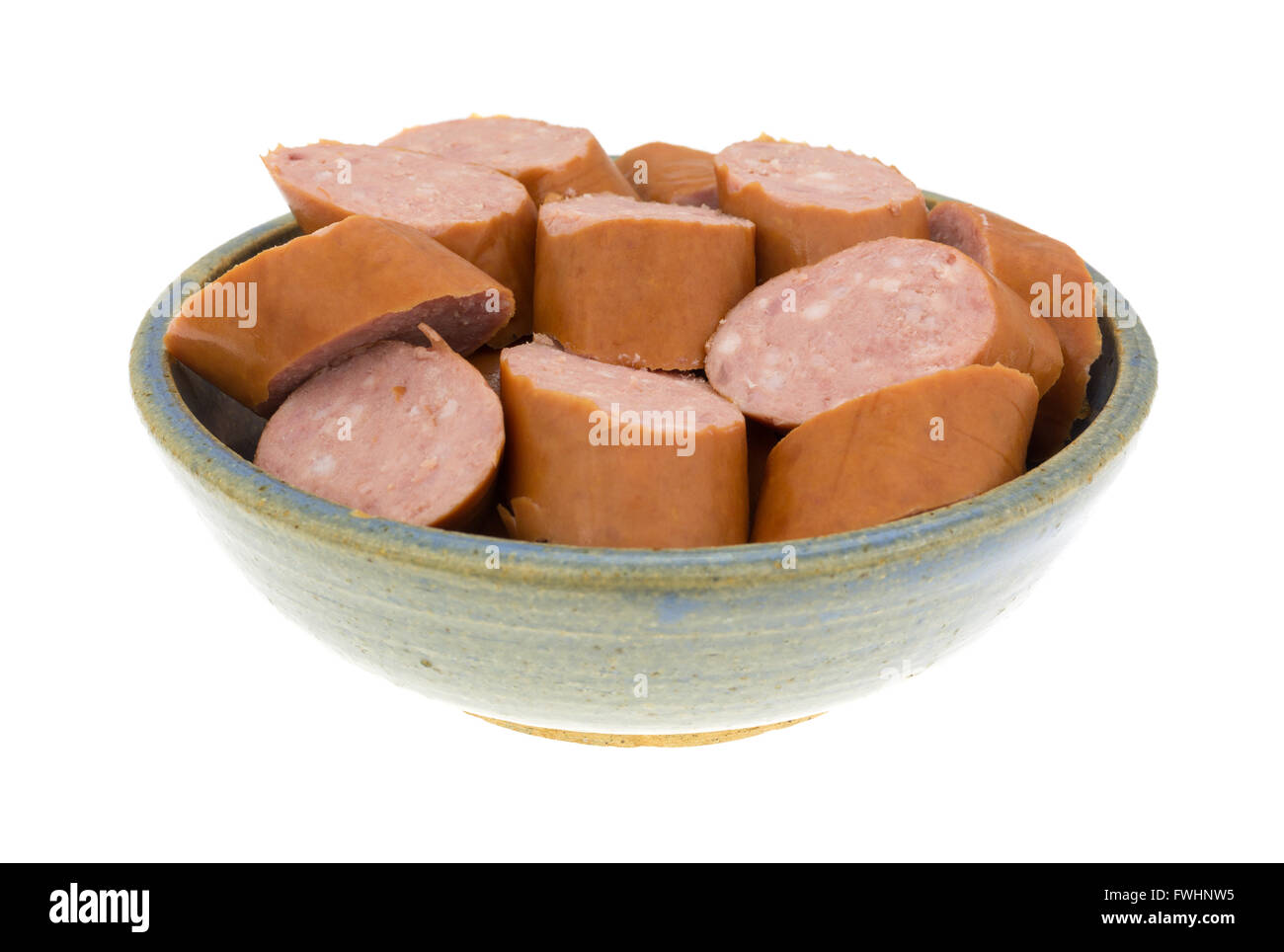 Several slices of reduced calorie kielbasa sausage in an old stoneware bowl isolated on a white background. Stock Photo