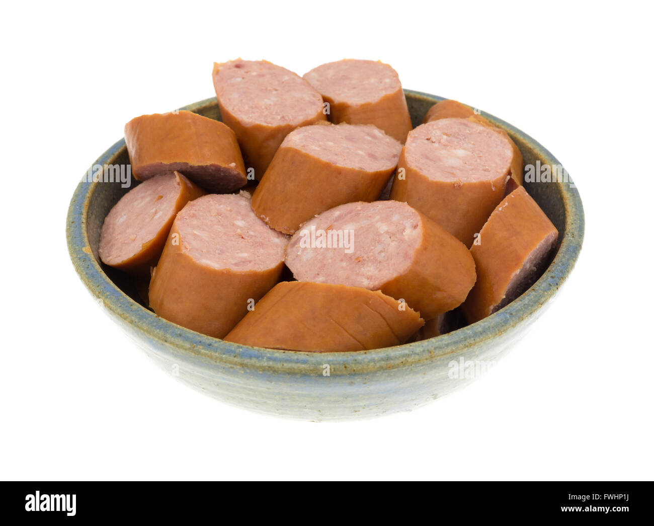 Several slices of reduced calorie kielbasa sausage in an old stoneware bowl isolated on a white background. Stock Photo
