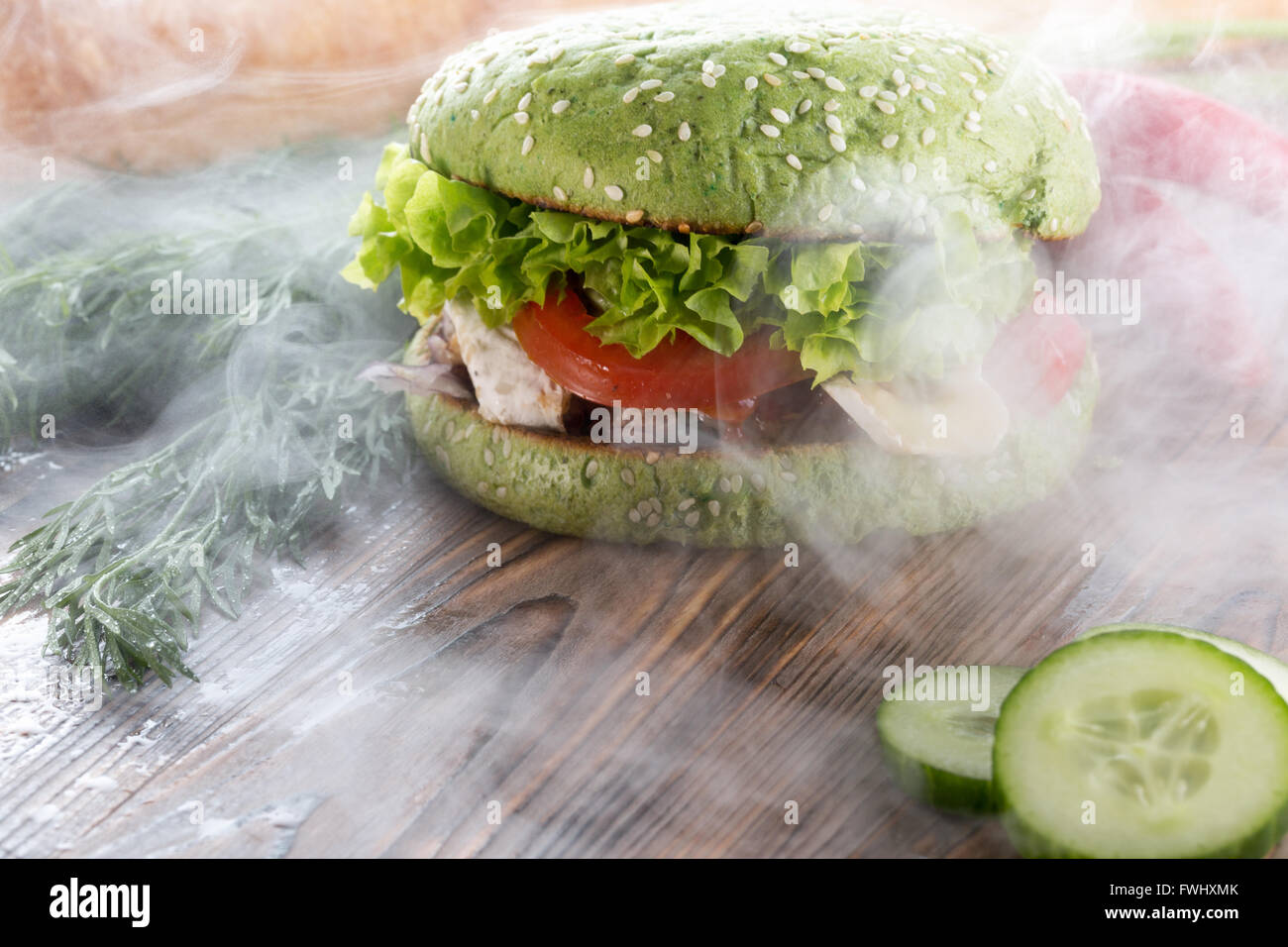 burger with green bun in light smoke on wooden background. Stock Photo