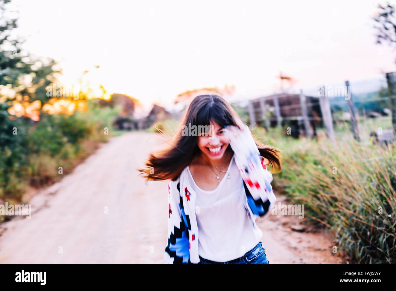 Portrait Of Happy Young Woman Running On Road Amidst Plants Against Clear Sky Stock Photo