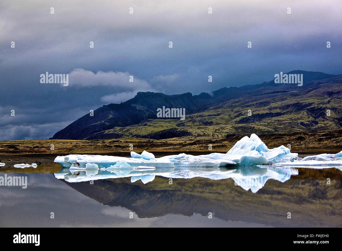 Ice Floating In River By Mountains Against Cloudy Sky Stock Photo