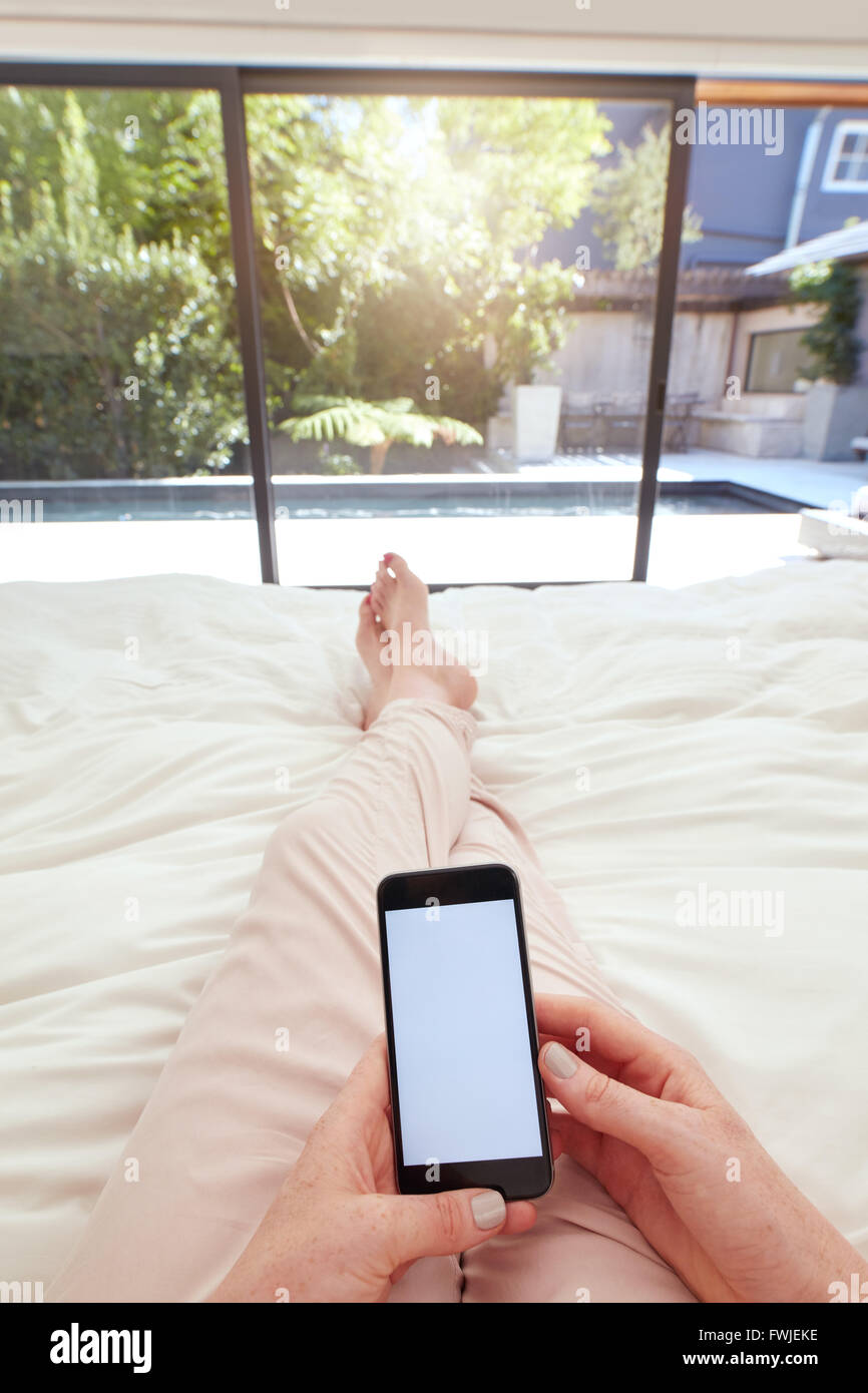 POV shot of a woman using mobile phone while lying on bed. Human hand  holding smart phone with blank screen in bedroom Stock Photo - Alamy