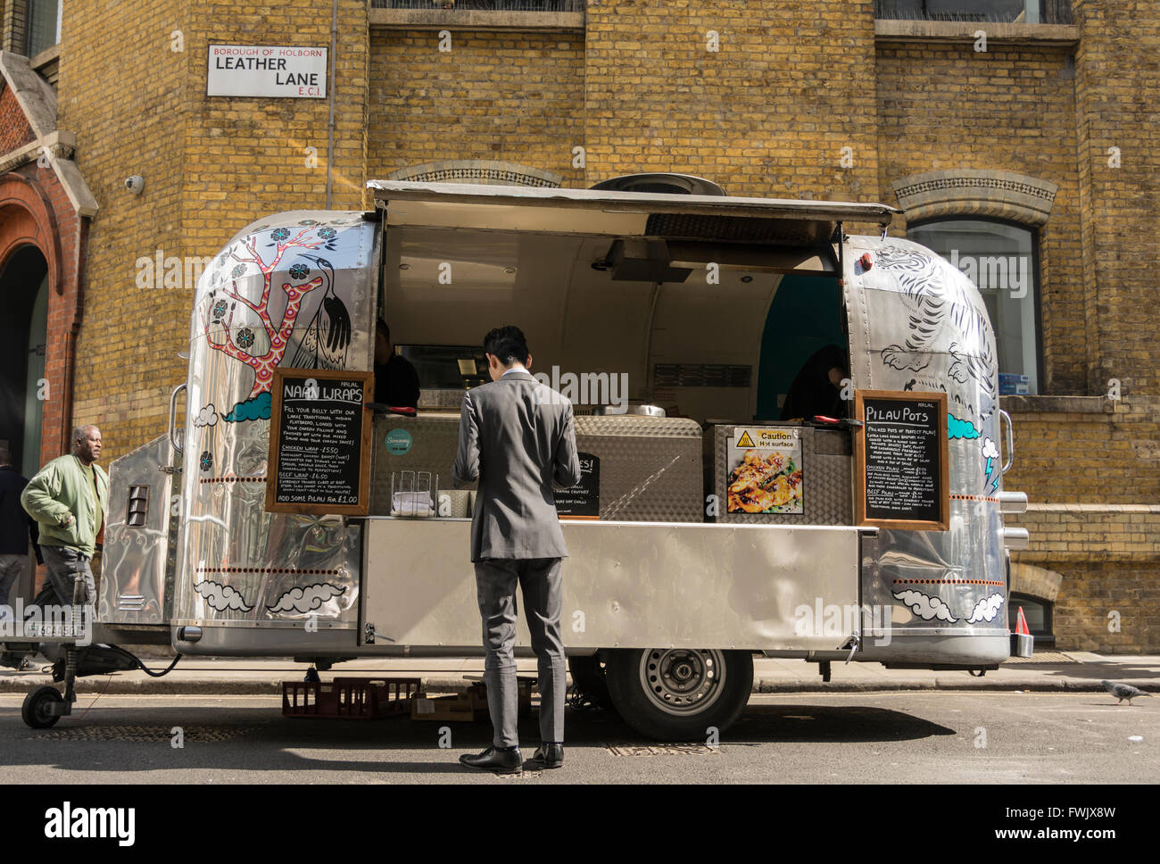 A smartly dressed man purchases a Naan wrap from a shiny Revival Trailer street stall seller on Leather Lane in London, UK. Stock Photo