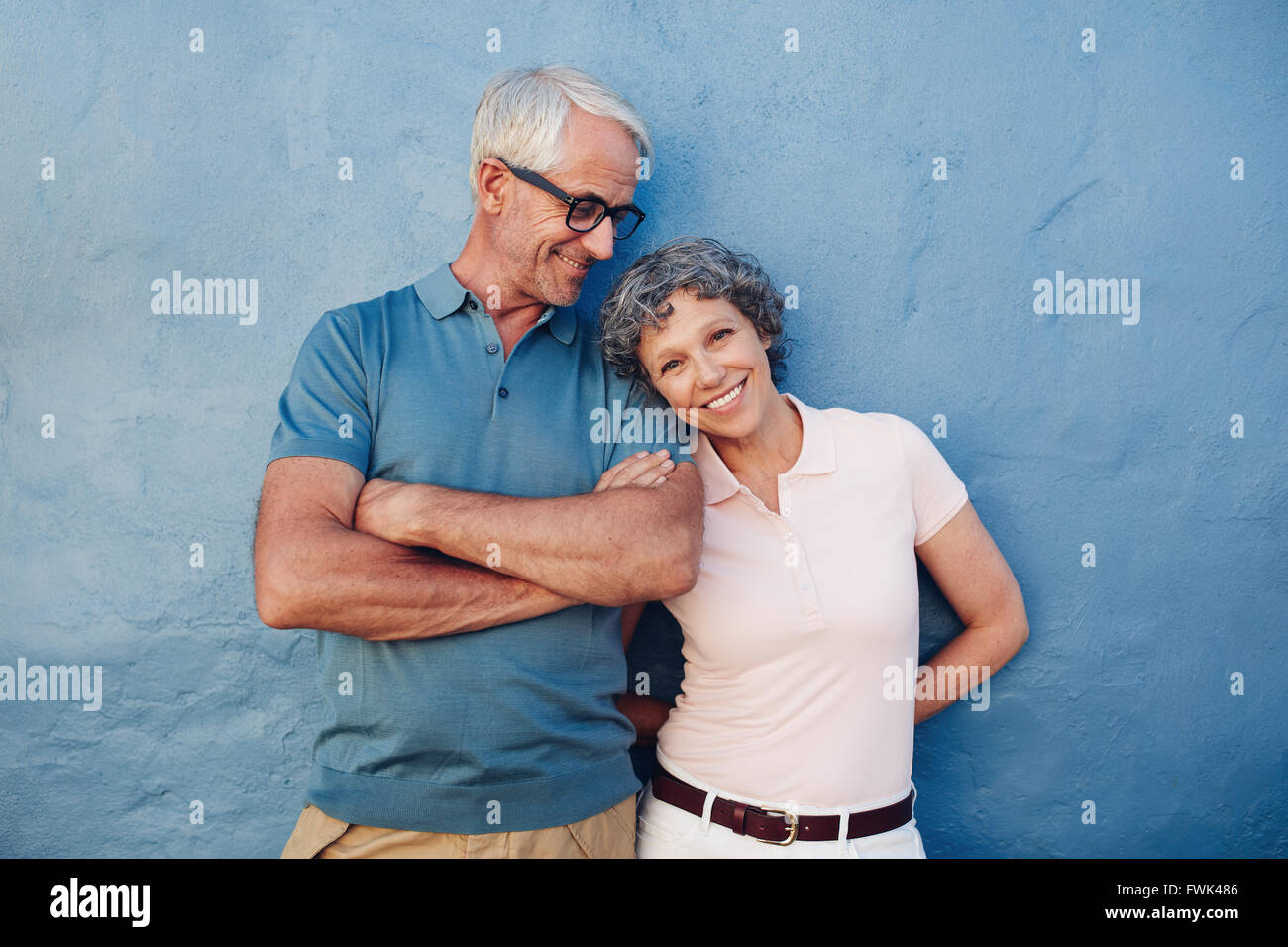Portrait of beautiful mature woman standing with her husband against blue background. Loving mature couple standing together aga Stock Photo