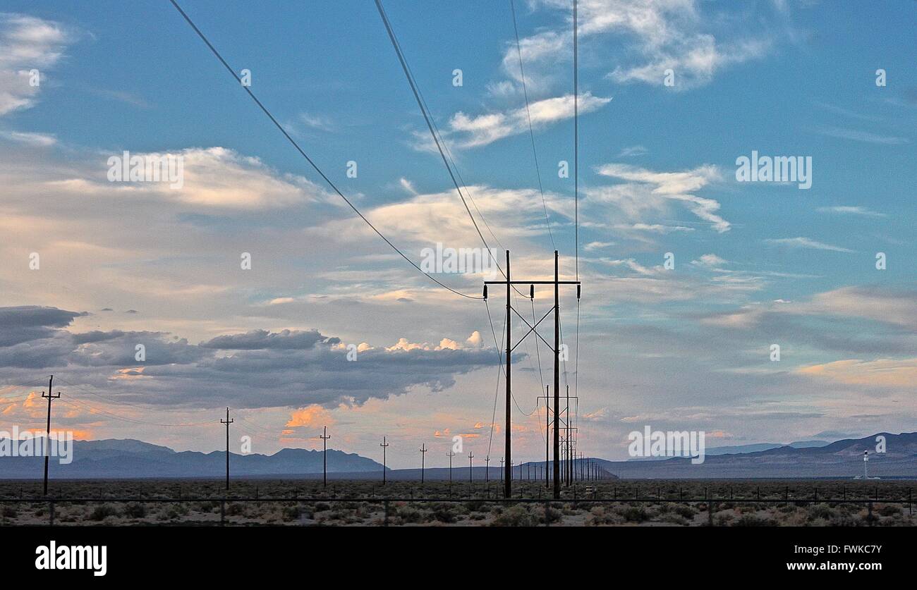 Electricity Pylons On Field Against Cloudy Sky Stock Photo