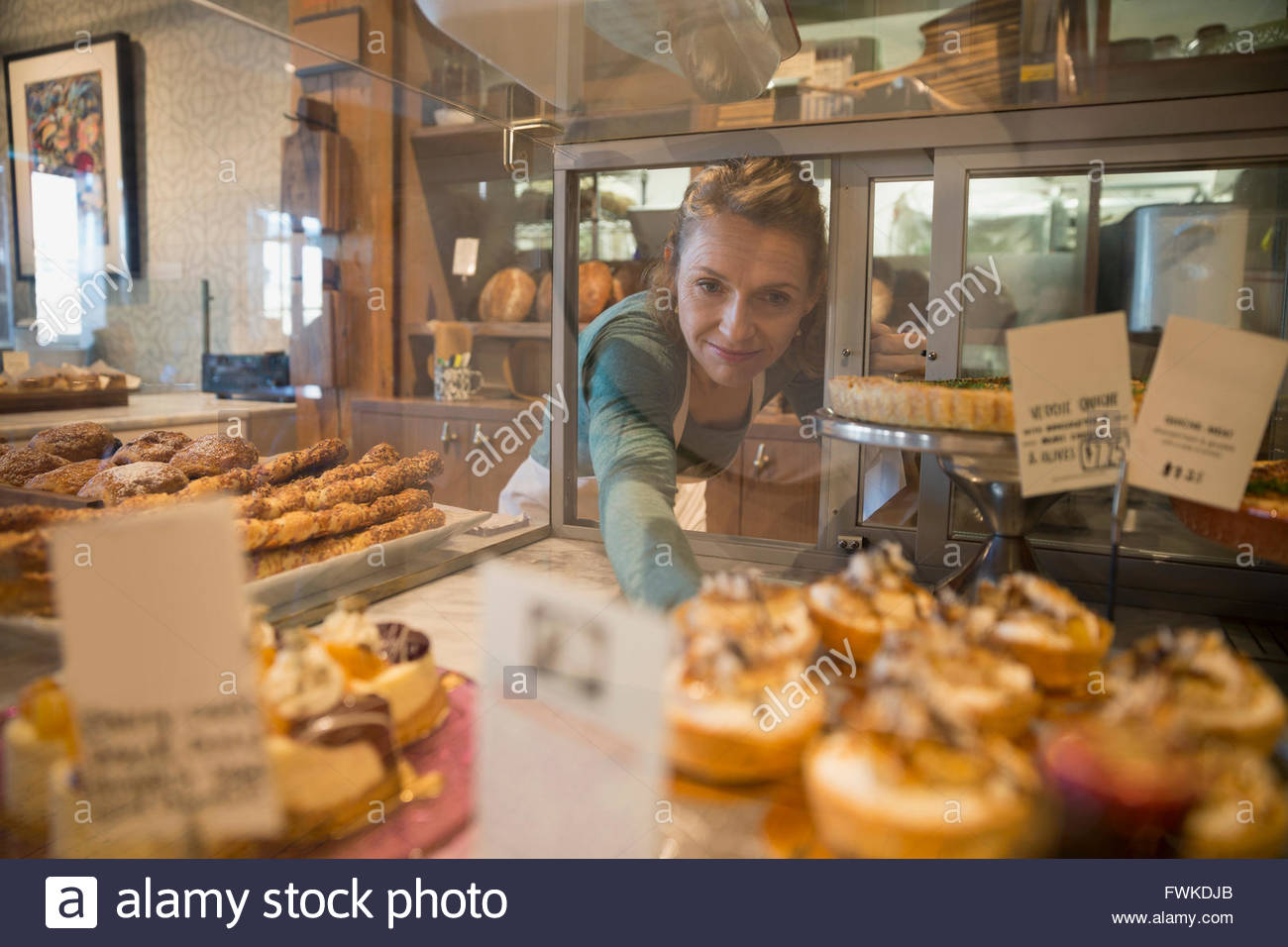 Bakery owner reaching for pastries in display case Stock Photo Alamy