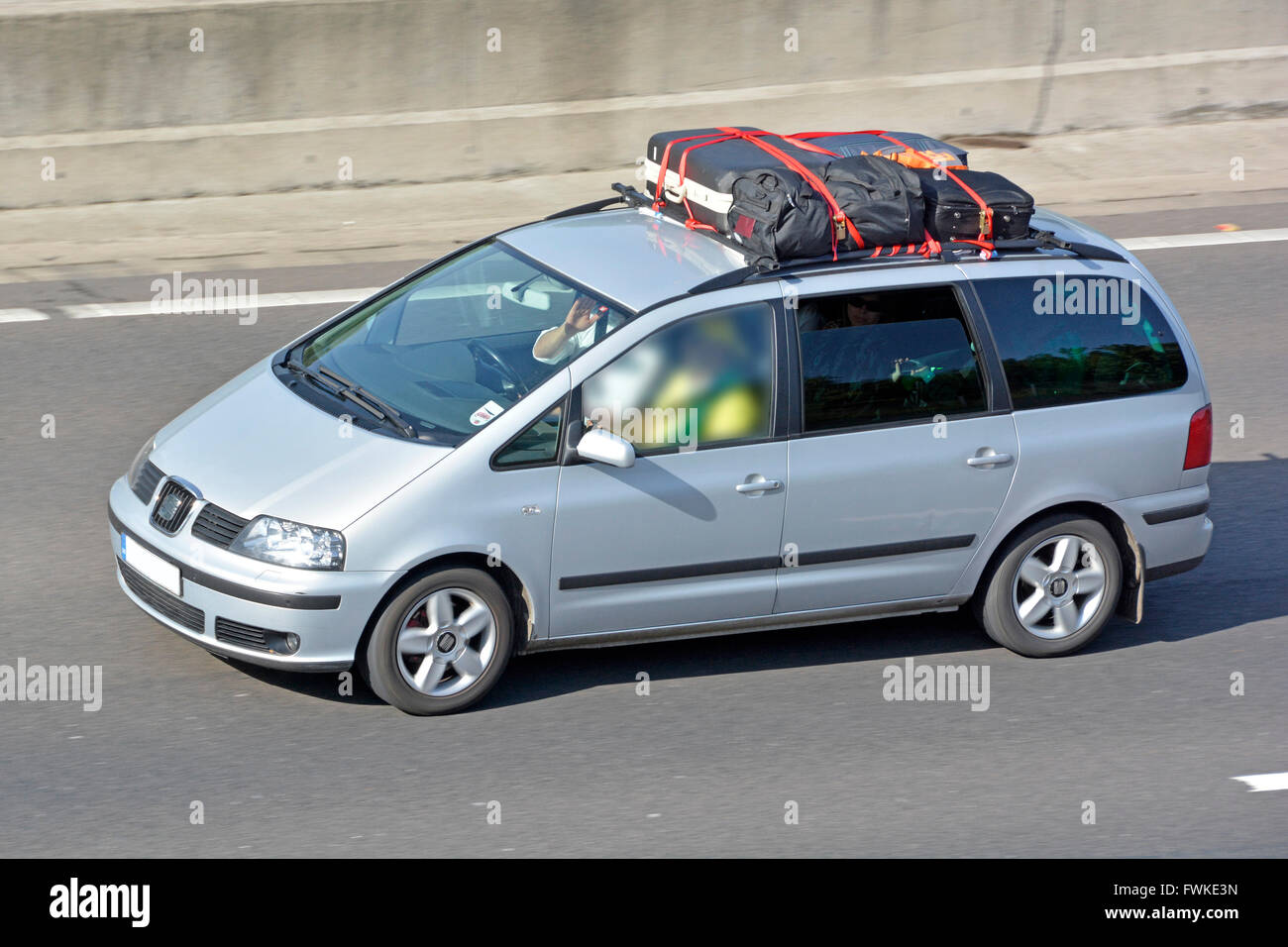 Car with loaded roof rack including suitcases driving along English UK motorway obscured passenger window central concrete crash barrier beyond Stock Photo