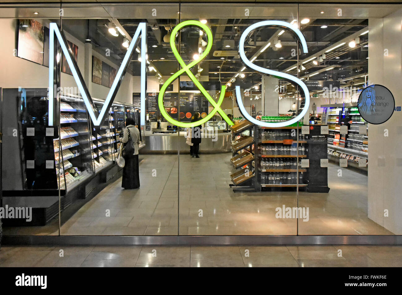 Foodhall beyond M&S illuminated store sign mounted on shop window of food hall in Westfield shopping centre Stratford City Newham East London England Stock Photo