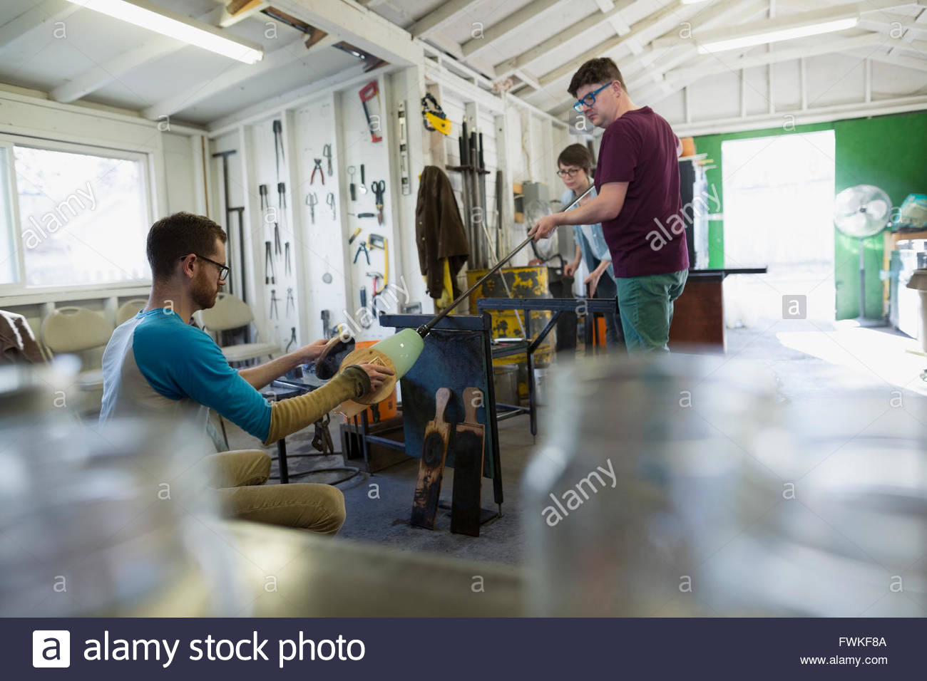 Glassblowers rolling and shaping glass in workshop Stock Photo