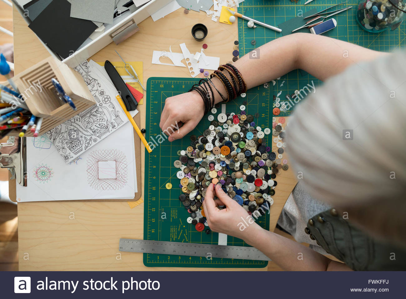 Overhead view craftswoman sorting buttons at desk Stock Photo