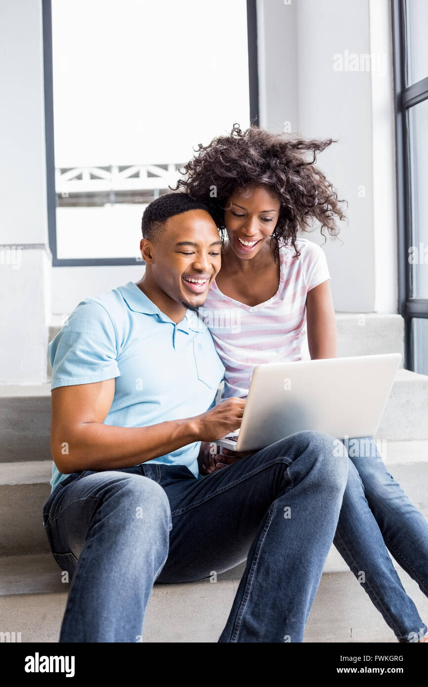 Happy couple sitting on steps and using laptop Stock Photo - Alamy