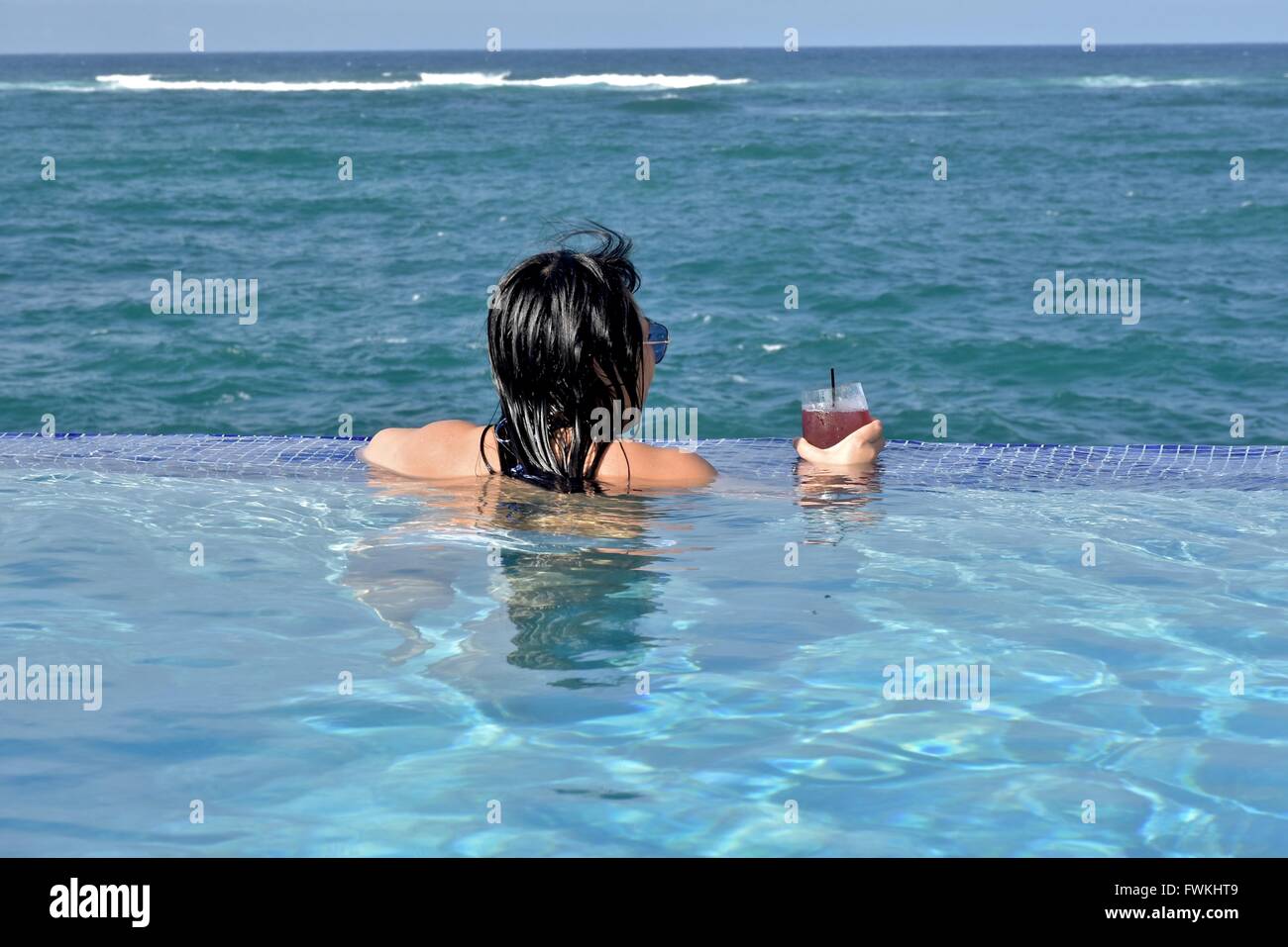 A woman in an infinity pool overlooking the ocean in Puerto Rico Stock Photo