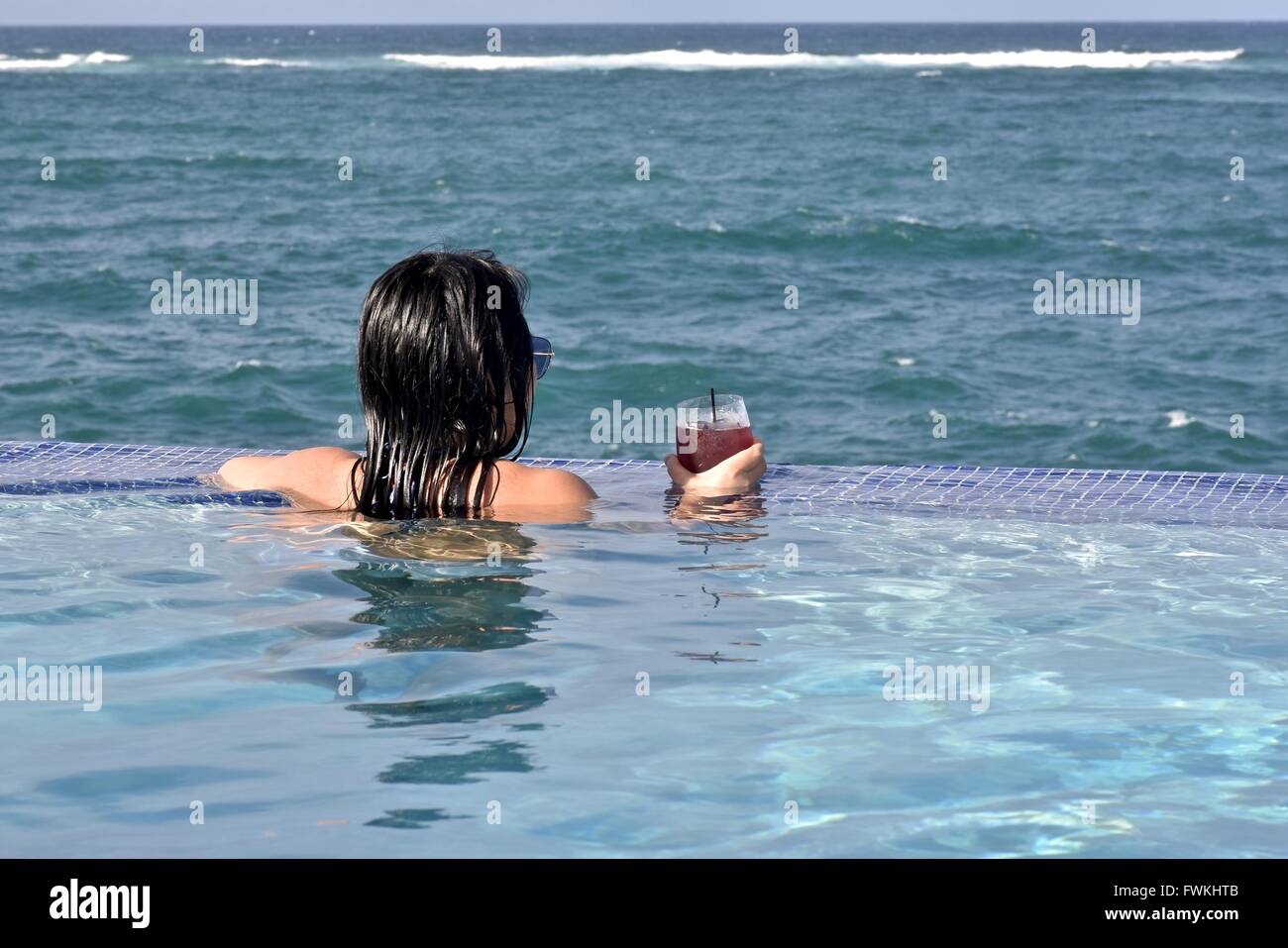 A woman in an infinity pool overlooking the ocean in Puerto Rico Stock Photo