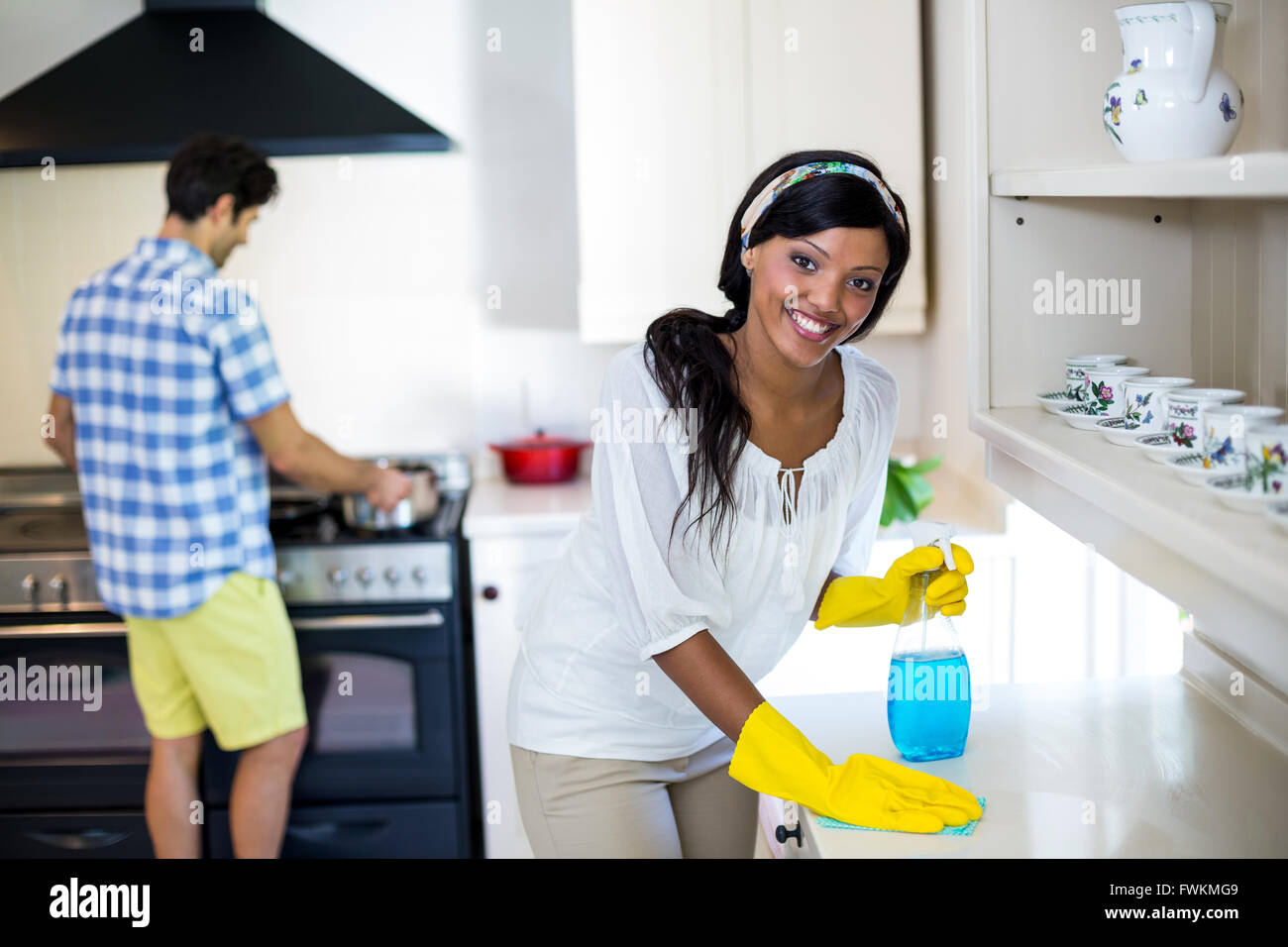 Woman cleaning the kitchen and man cooking food in background Stock