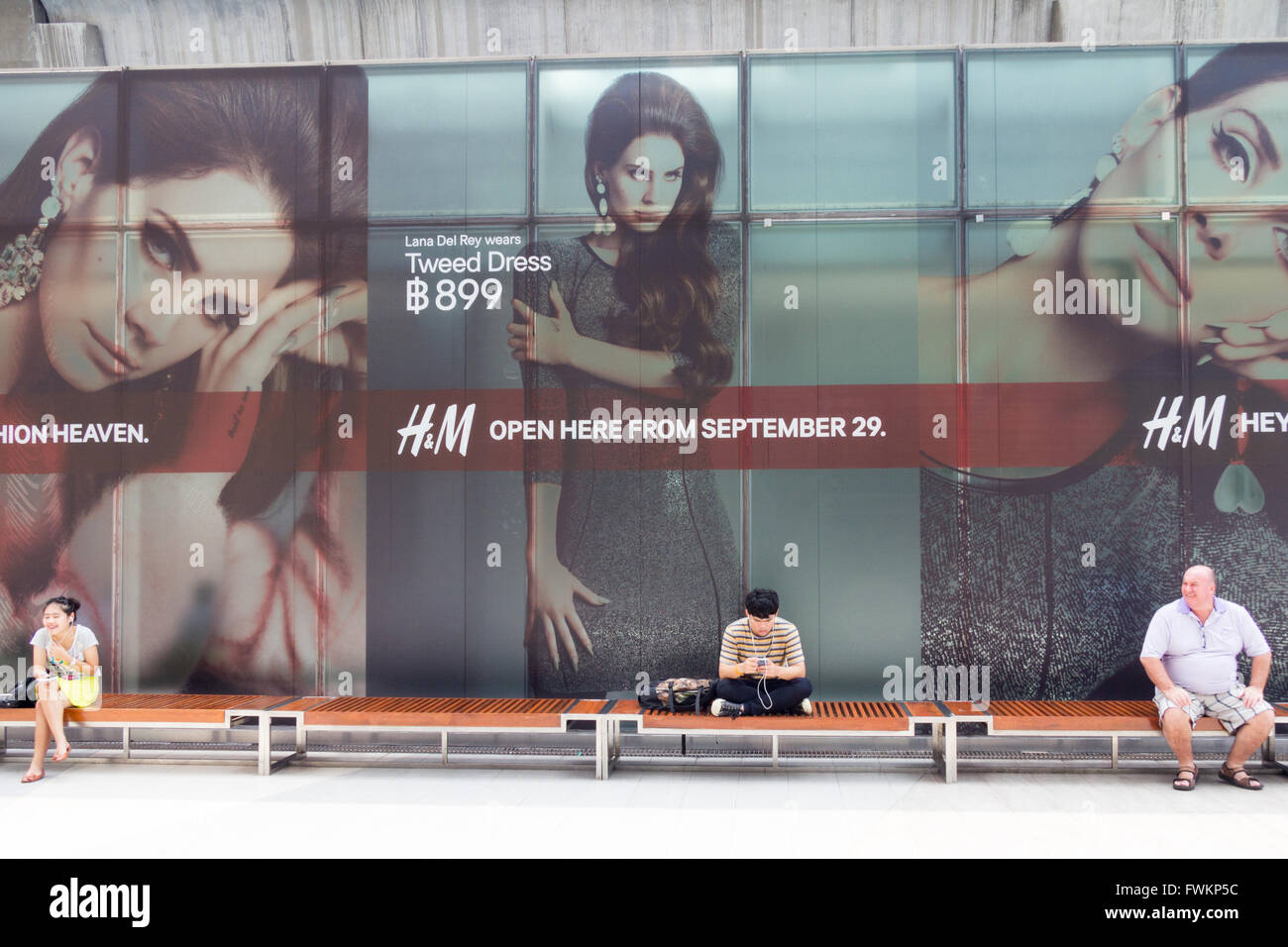 People sitting on a bench with an advertisement behind them for the opening  of a new H&M store in Siam Paragon Mall, Bangkok Stock Photo - Alamy