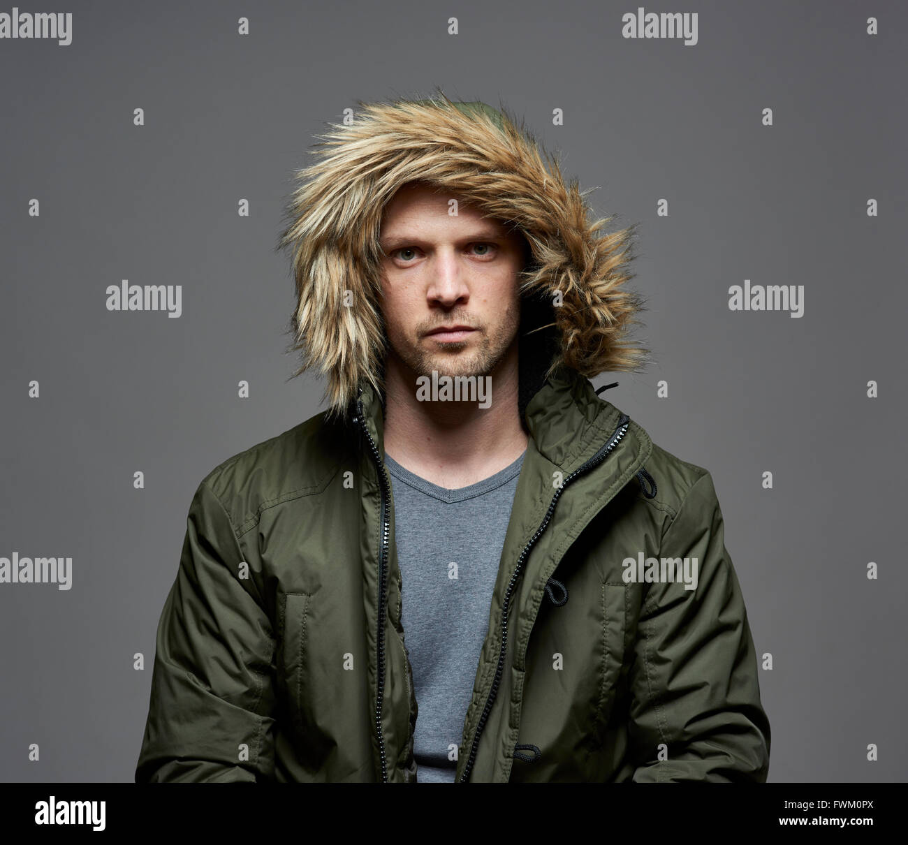 Studio portrait of young adult caucasian model wearing winter coat with hood on. Isolated on gray background. Stock Photo