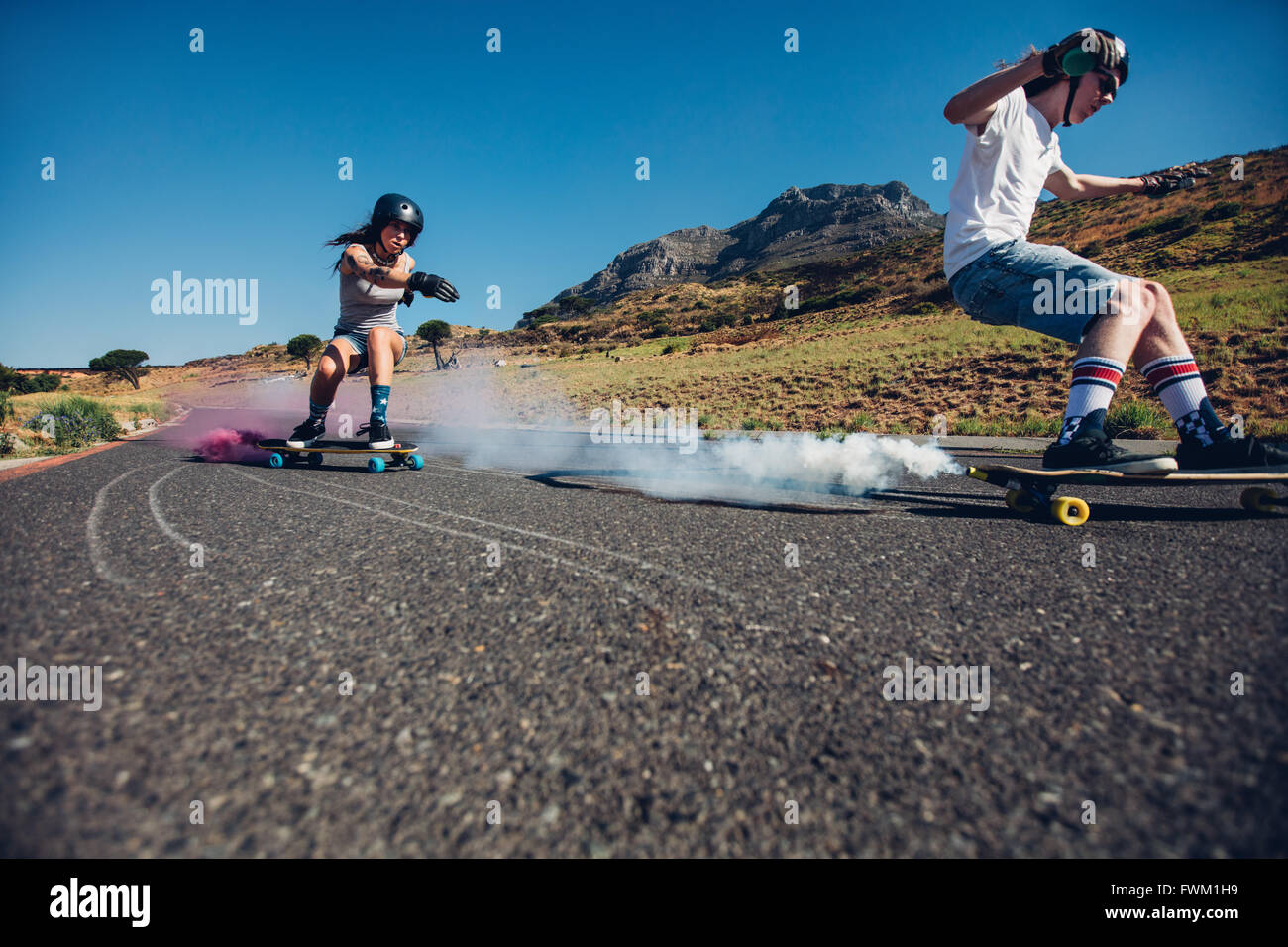 Young man and woman practicing skating on skateboard with smoke grenade. Teenagers longboarding on open road. Skate board with s Stock Photo
