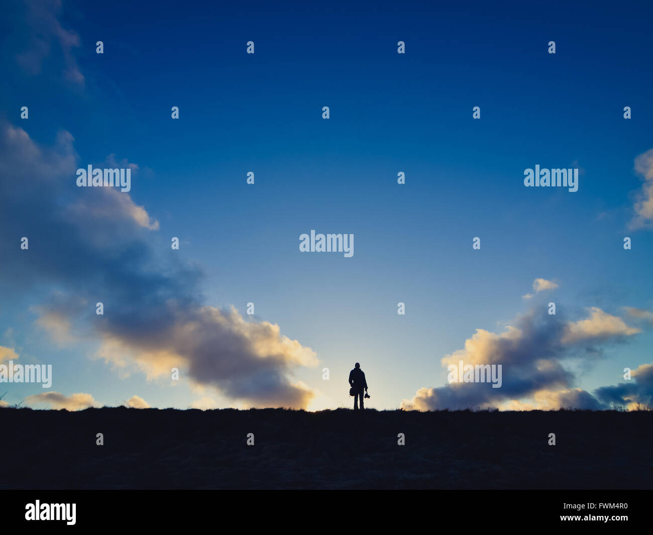 Distant View Of Silhouette Man On Field Against Sky At Sunset Stock Photo