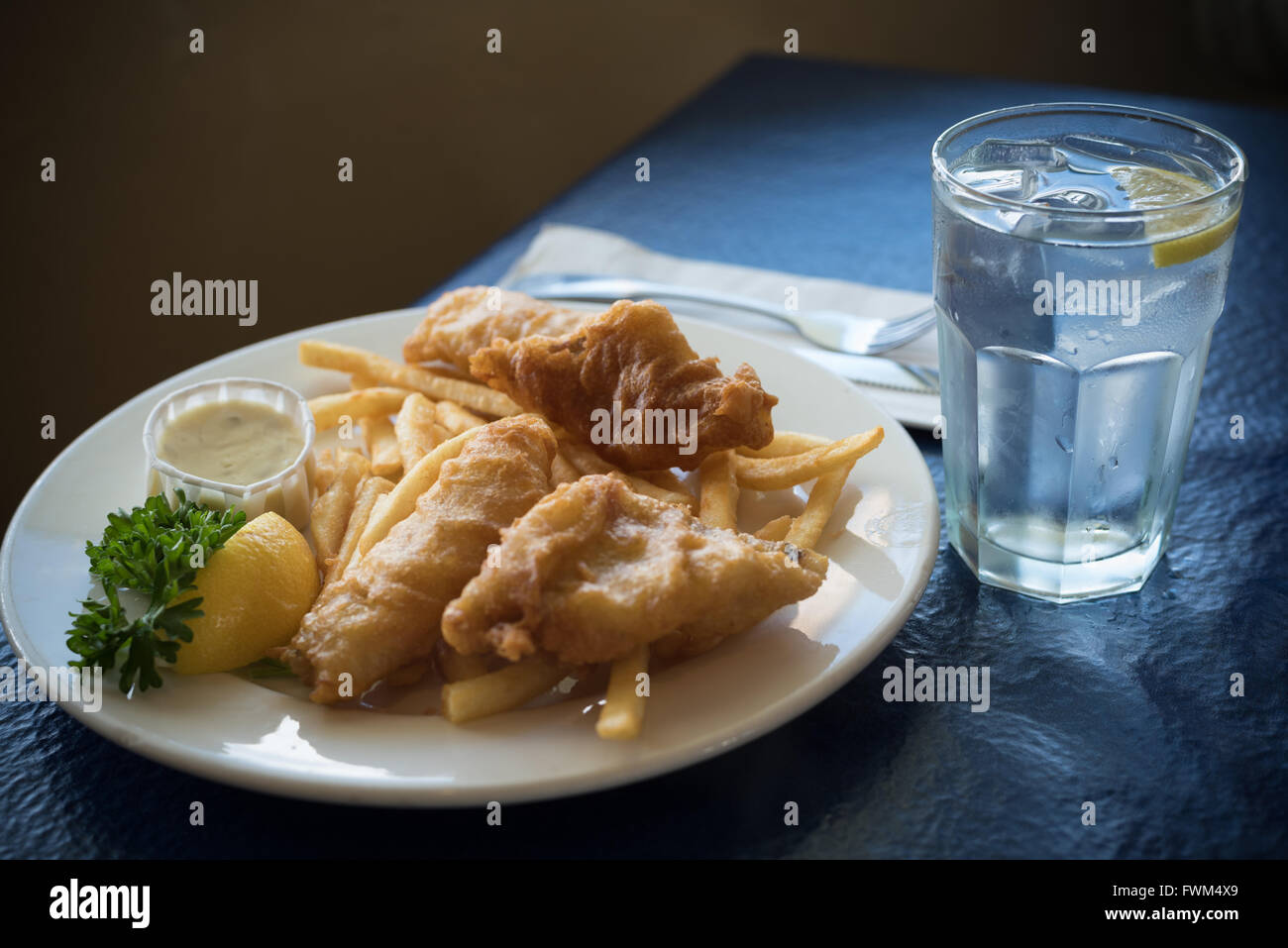 A plate of fried fish, cod or hallibut, with french fries or chips with a glass ow water Stock Photo