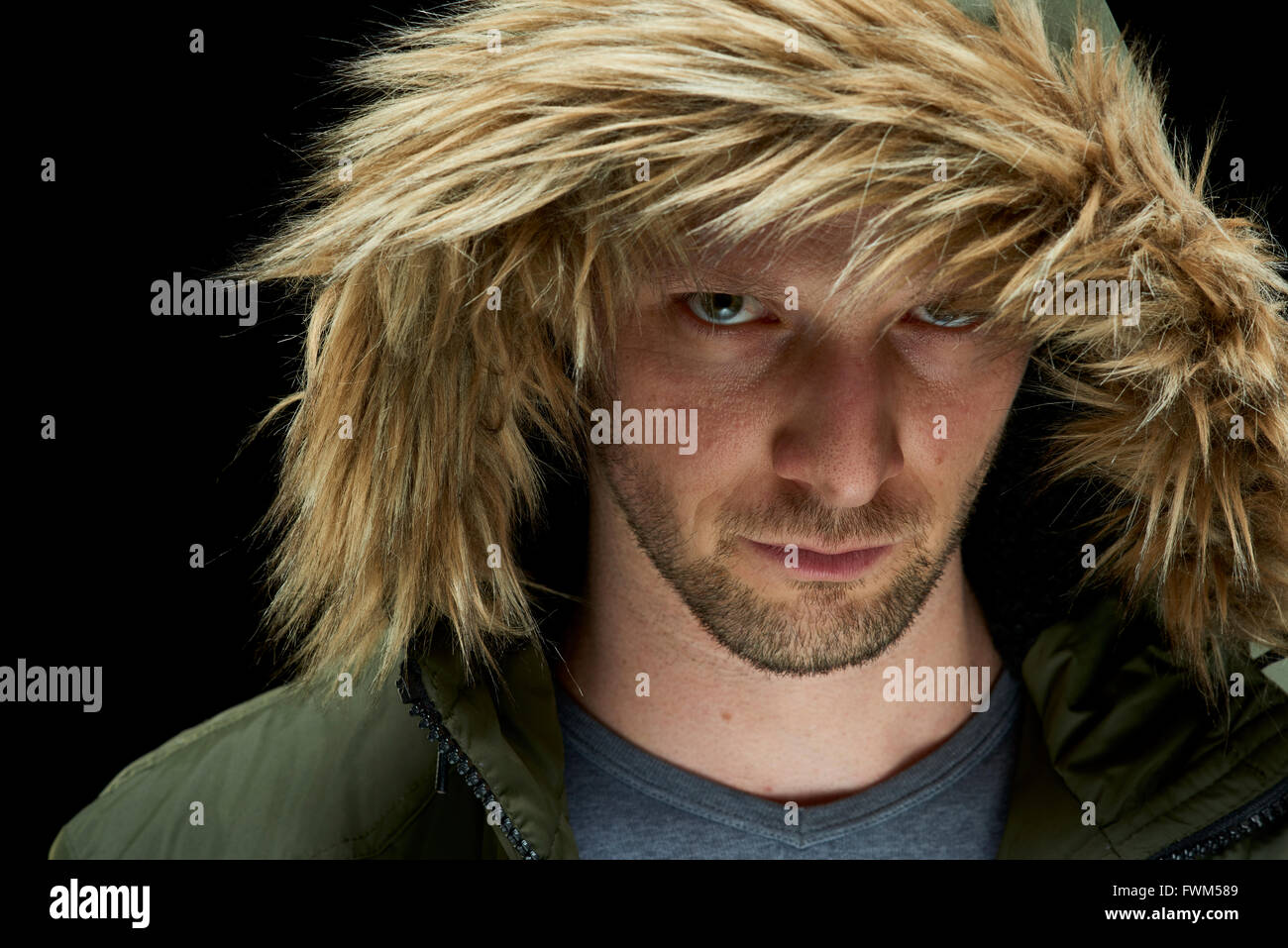Low key studio portrait of suspicious young adult caucasian model wearing winter coat with hood on. Stock Photo