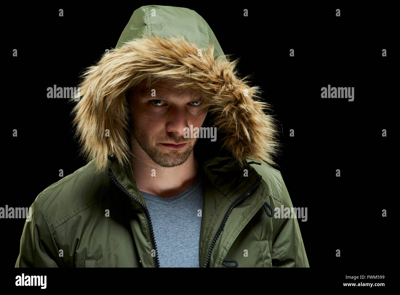 Low key studio portrait of suspicious young adult caucasian model wearing winter coat with hood on. Stock Photo