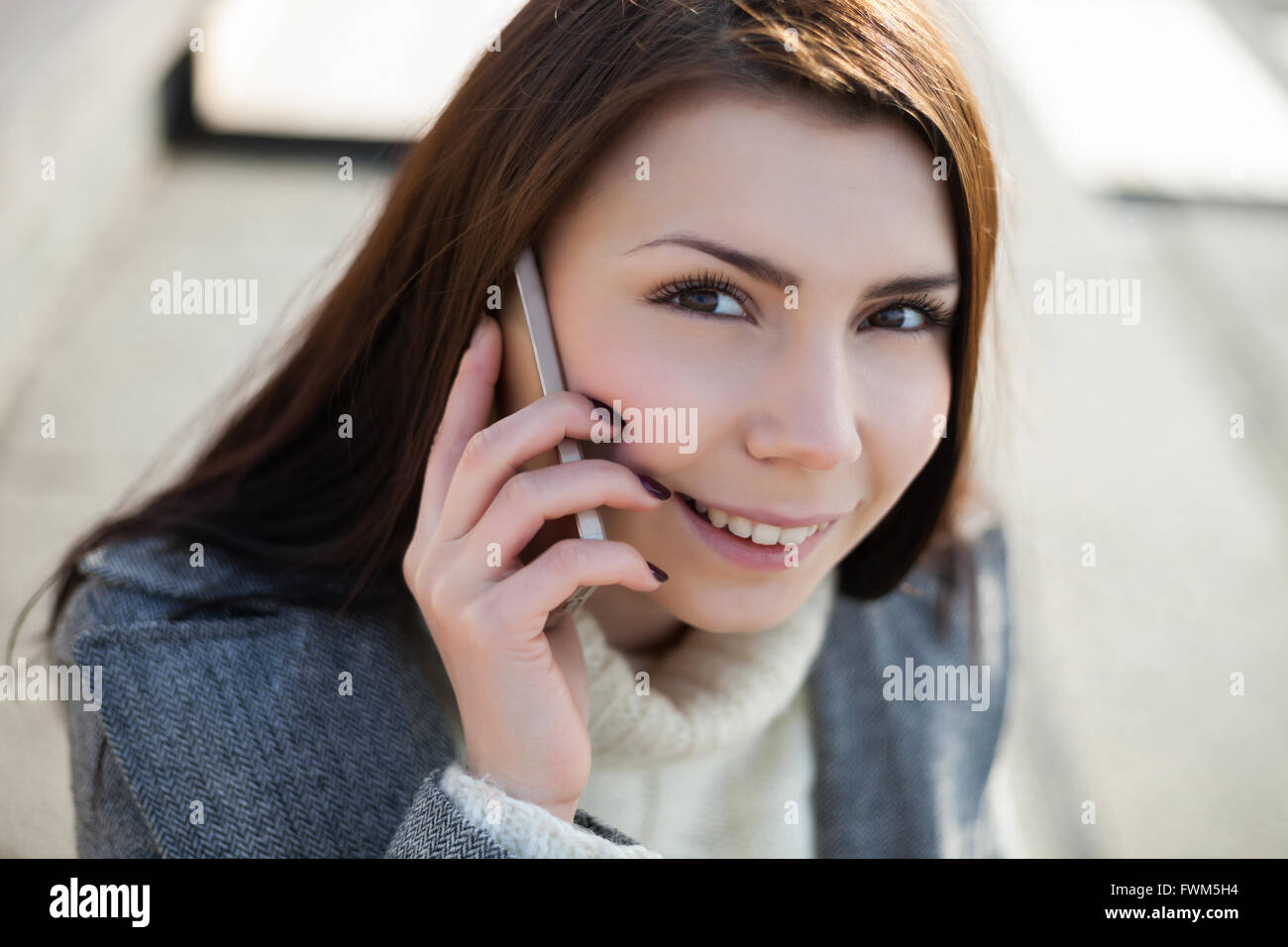 Cute young girl with pug nose talking on the phone at bright spring day outdoors. The model is beautiful and the smart phone is modern Stock Photo