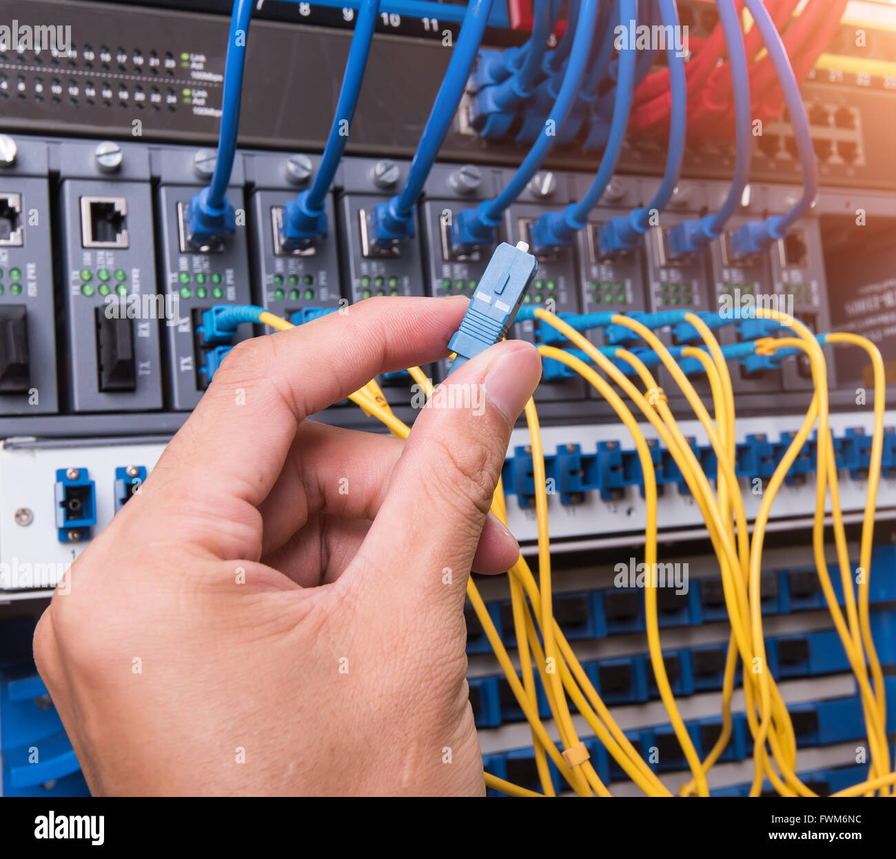 man working in network server room with fiber optic hub for digital ...