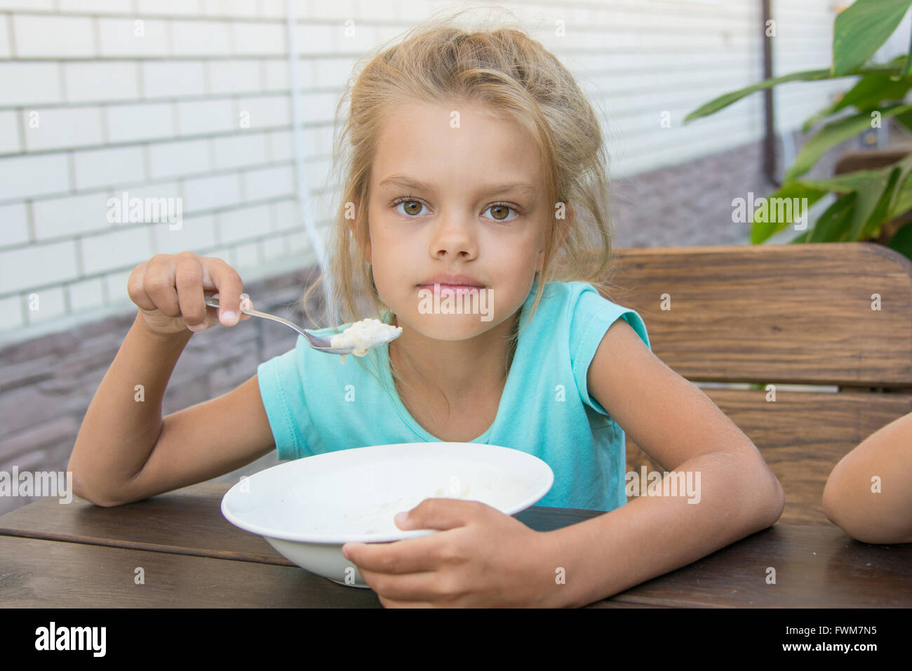 Six year old girl at a wooden table in the yard eating porridge Stock