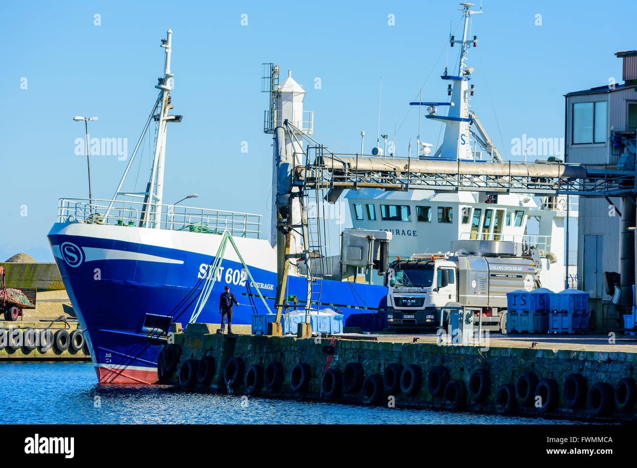 Simrishamn, Sweden - April 1, 2016: A man pull a rope to open the ice flow down to blue crates. Fishing boat behind him and a tr Stock Photo