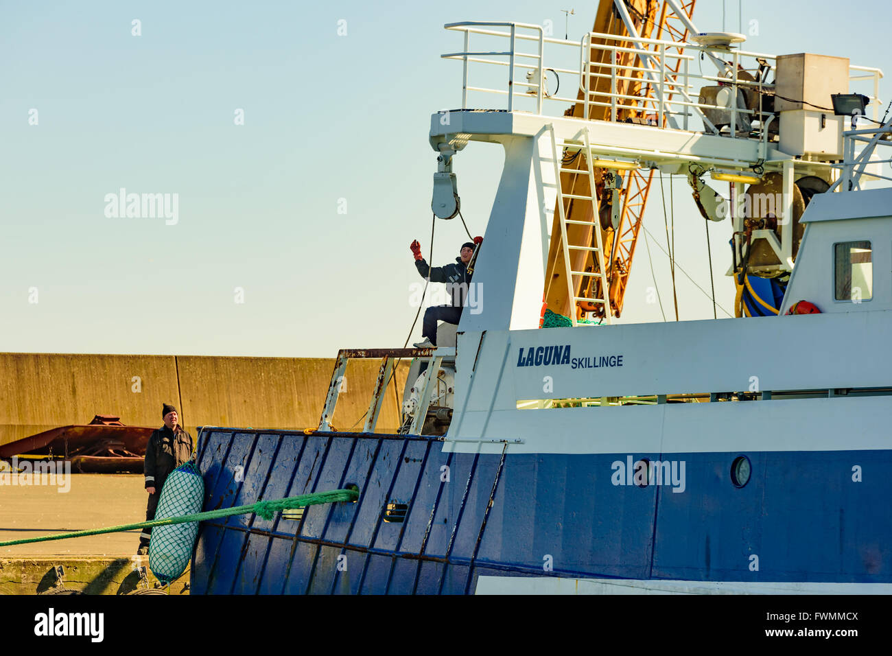 Simrishamn, Sweden - April 1, 2016: Two persons work on and beside a fishing boat, getting a rope on a cylinder. One of them is Stock Photo
