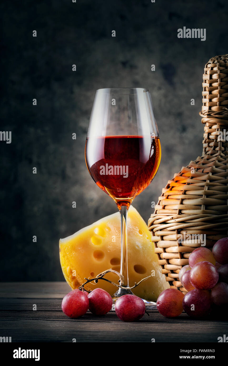 Glass of red wine with grapes and wicker bottle on dark background Stock Photo