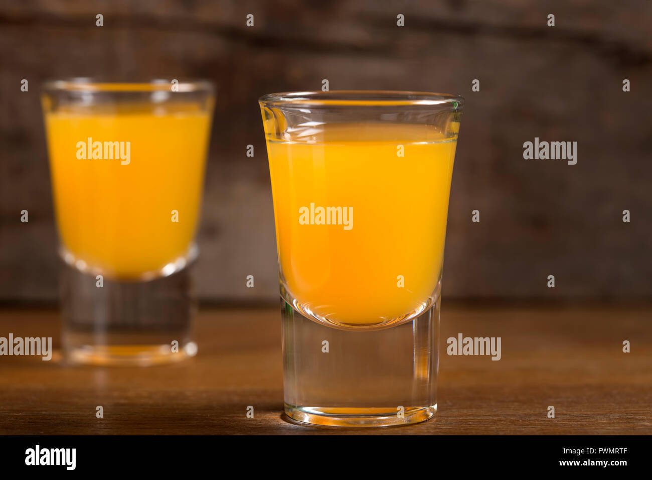 Two shot glasses of vodka with orange juice over wooden background Stock Photo