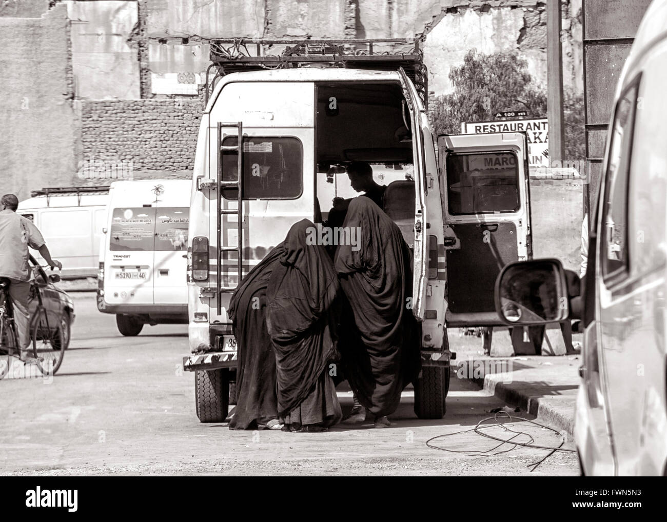 Three women in black burka entering taxi bus in Morocco Stock Photo
