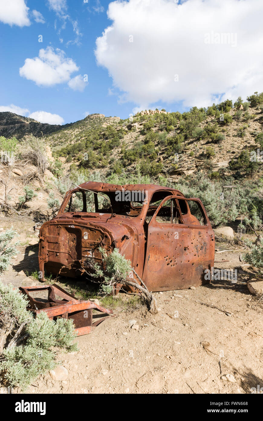 A rusty car wreck riddled with bullet holes lies rusting near Sego ghost town, Utah, USA Stock Photo