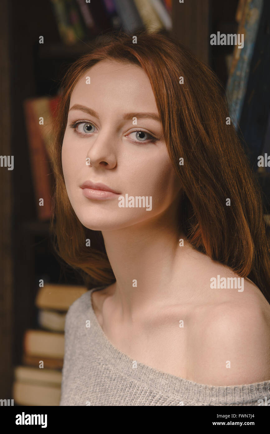 Redhair girl in grey pullover standing in book library. Close up portrait. Stock Photo