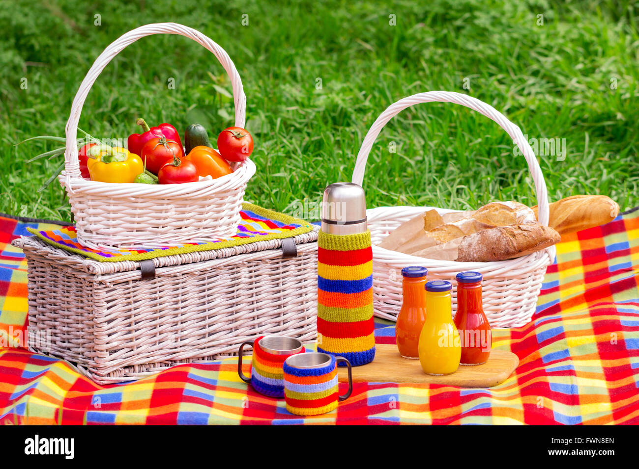 Picnic on the grass. Picnic basket with vegetables and bread. A thermos of tea and bottles of juice. Stock Photo