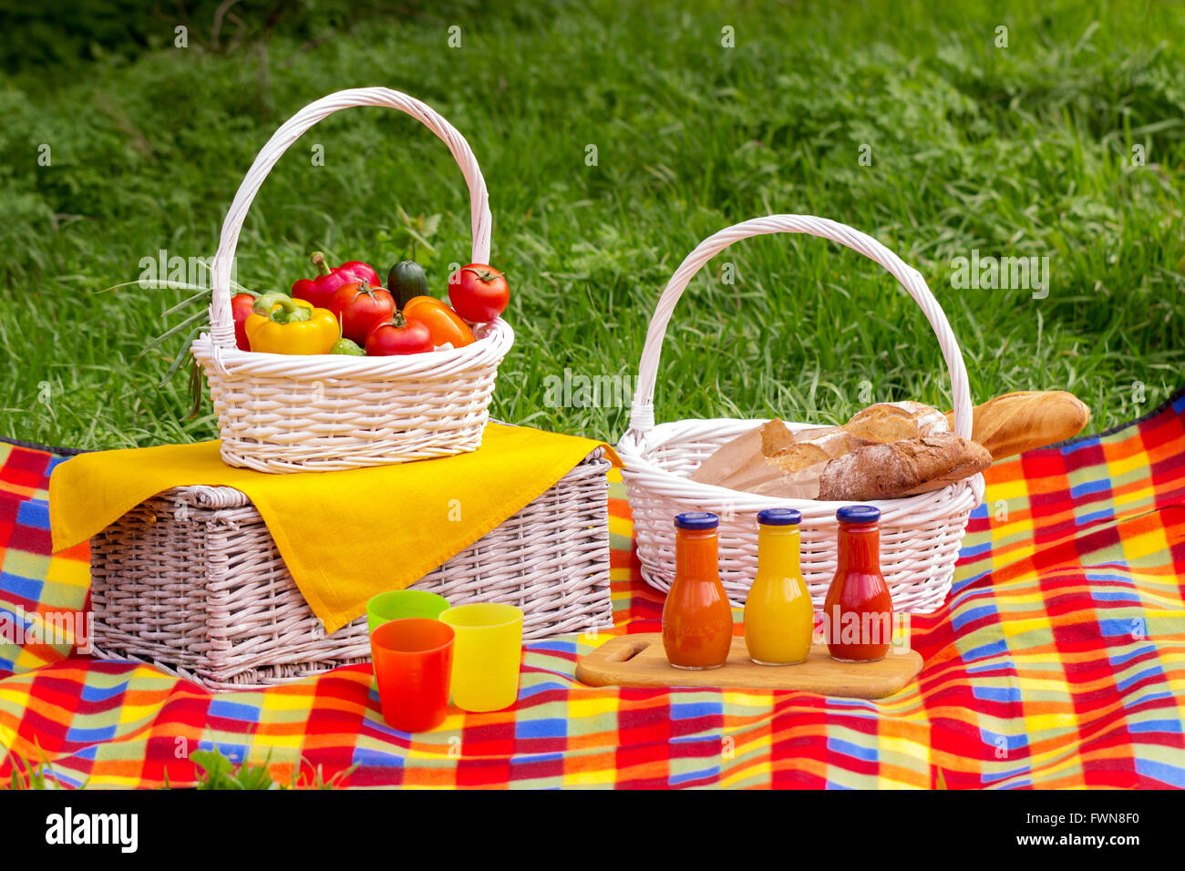 Picnic on the grass. Picnic basket with vegetables and bread. A bottles of juice. Stock Photo