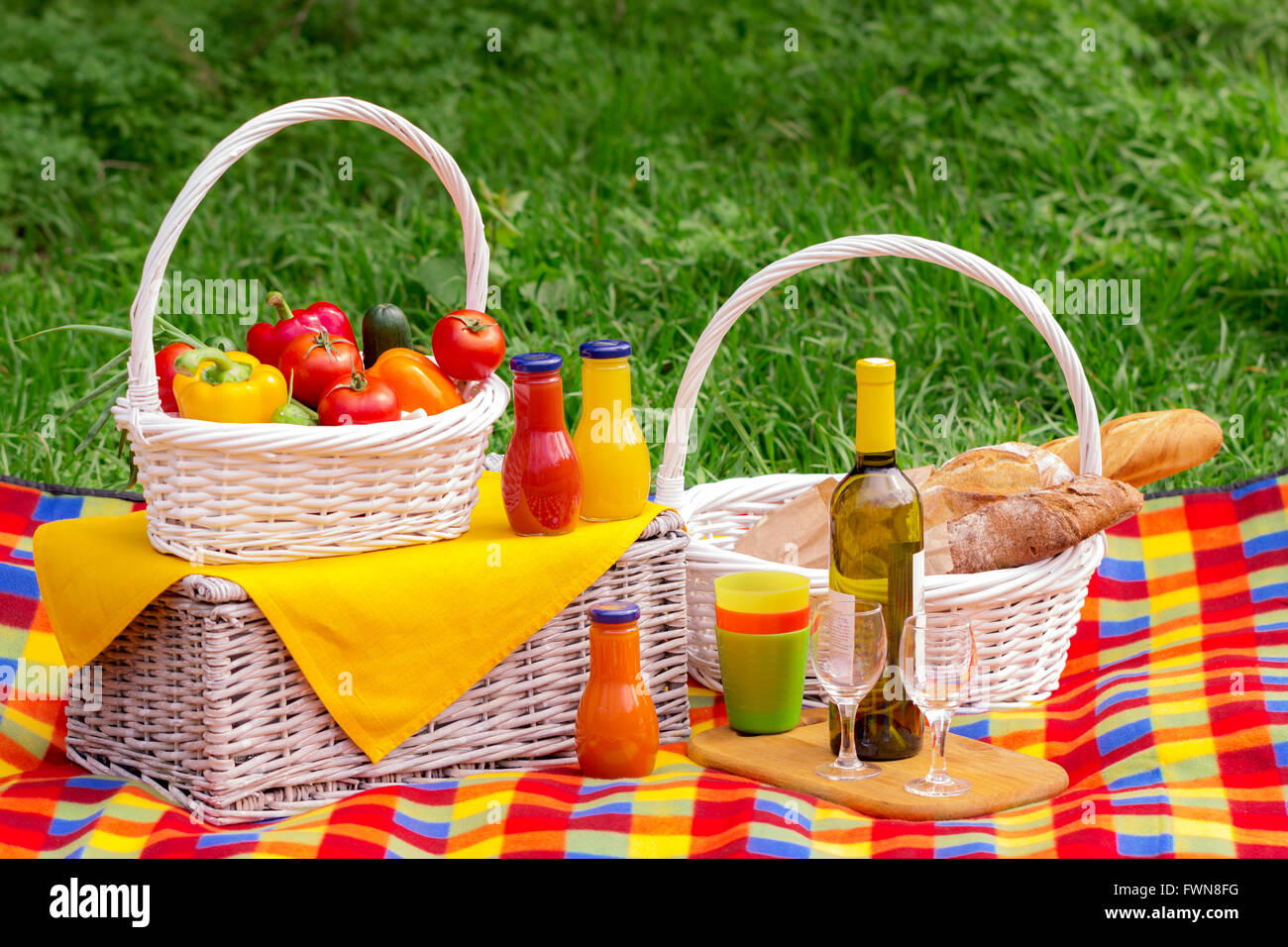 Picnic on the grass. Picnic basket with vegetables and bread. A bottle of wine with glasses and bottles of juice. Stock Photo