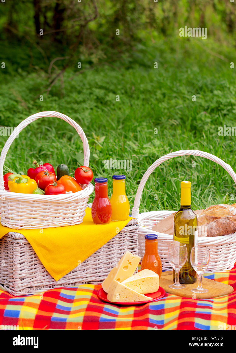Picnic on the grass. Picnic basket with vegetables and bread. A bottle of wine with glasses and bottles of juice. Stock Photo