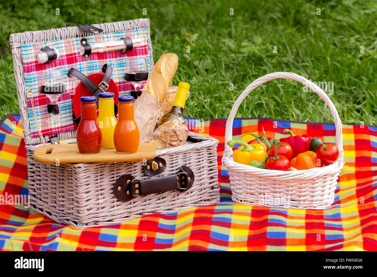 Picnic on the grass. Picnic basket with vegetables and bread. A bottle of wine and bottles of juice. Stock Photo