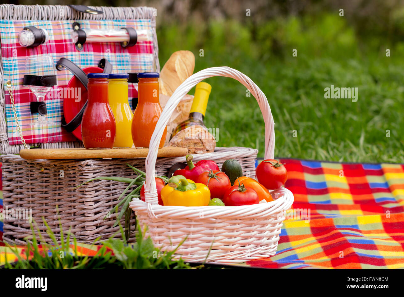 Picnic on the grass. Picnic basket with vegetables and bread. A bottle of wine and bottles of juice. Stock Photo