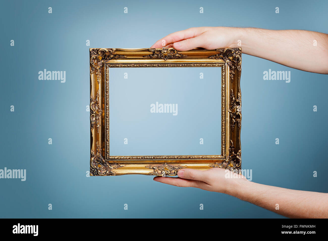 Man holding an antique style golden frame in his hands. Stock Photo