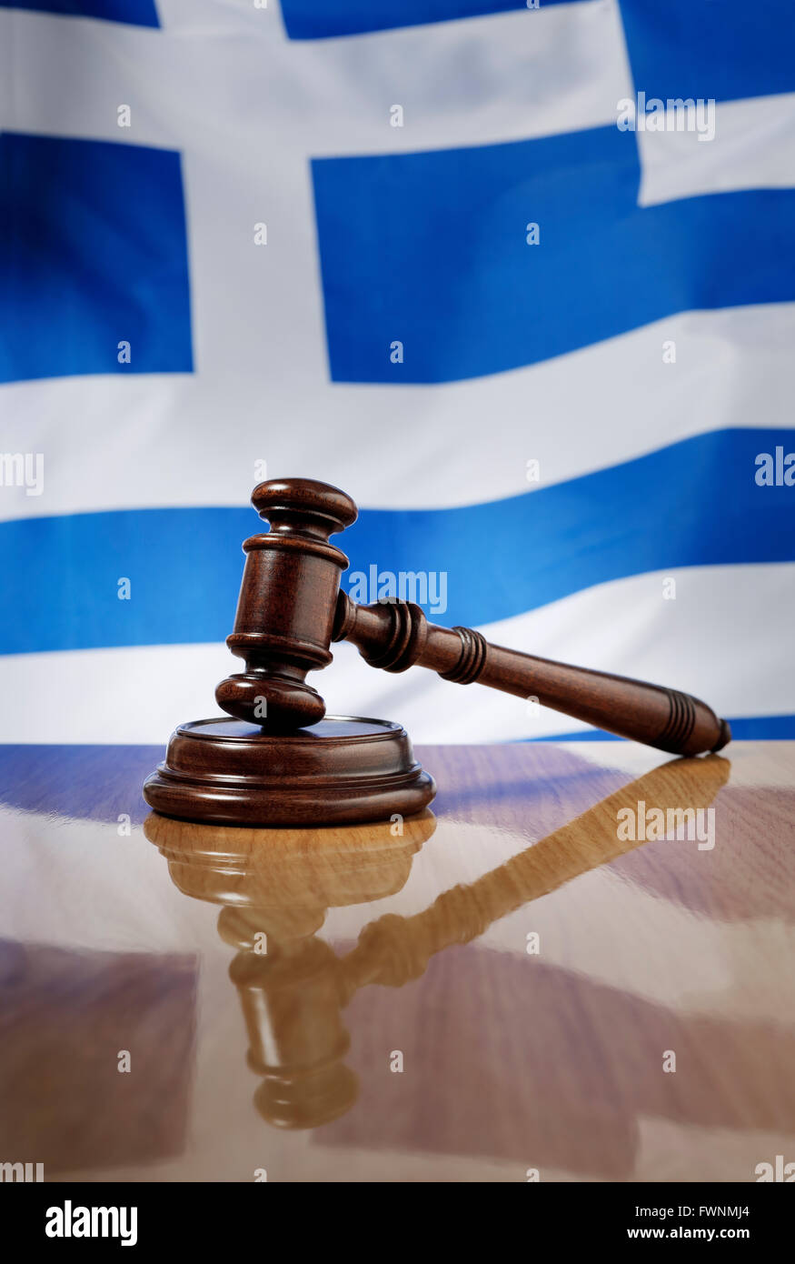 Mahogany wooden gavel on glossy wooden table, flag of Greece in the background. Stock Photo