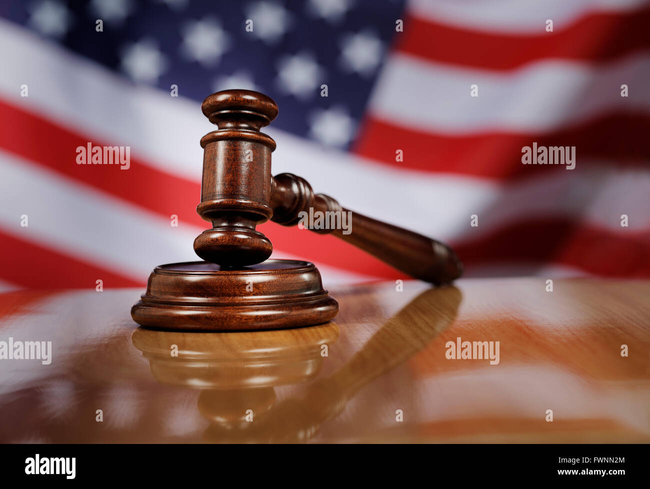 Mahogany wooden gavel on glossy wooden table, USA flag in the background. Stock Photo