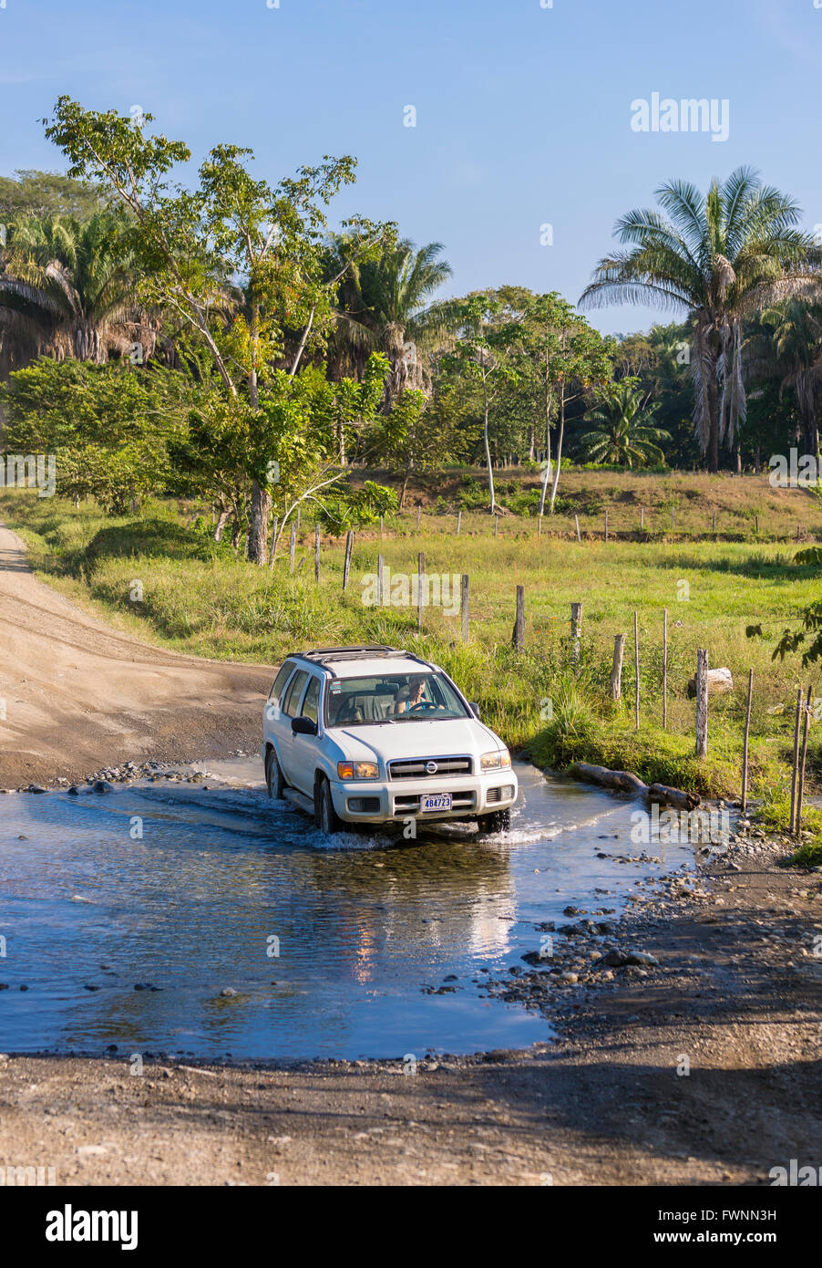 OSA PENINSULA, COSTA RICA - Car fords stream across dirt road. Stock Photo