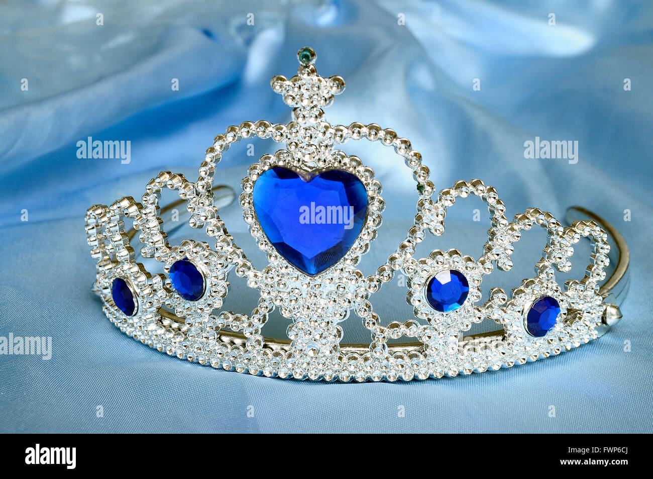 Toy tiara with diamonds and blue gem, like a princess crown, on blue satin tissue Stock Photo