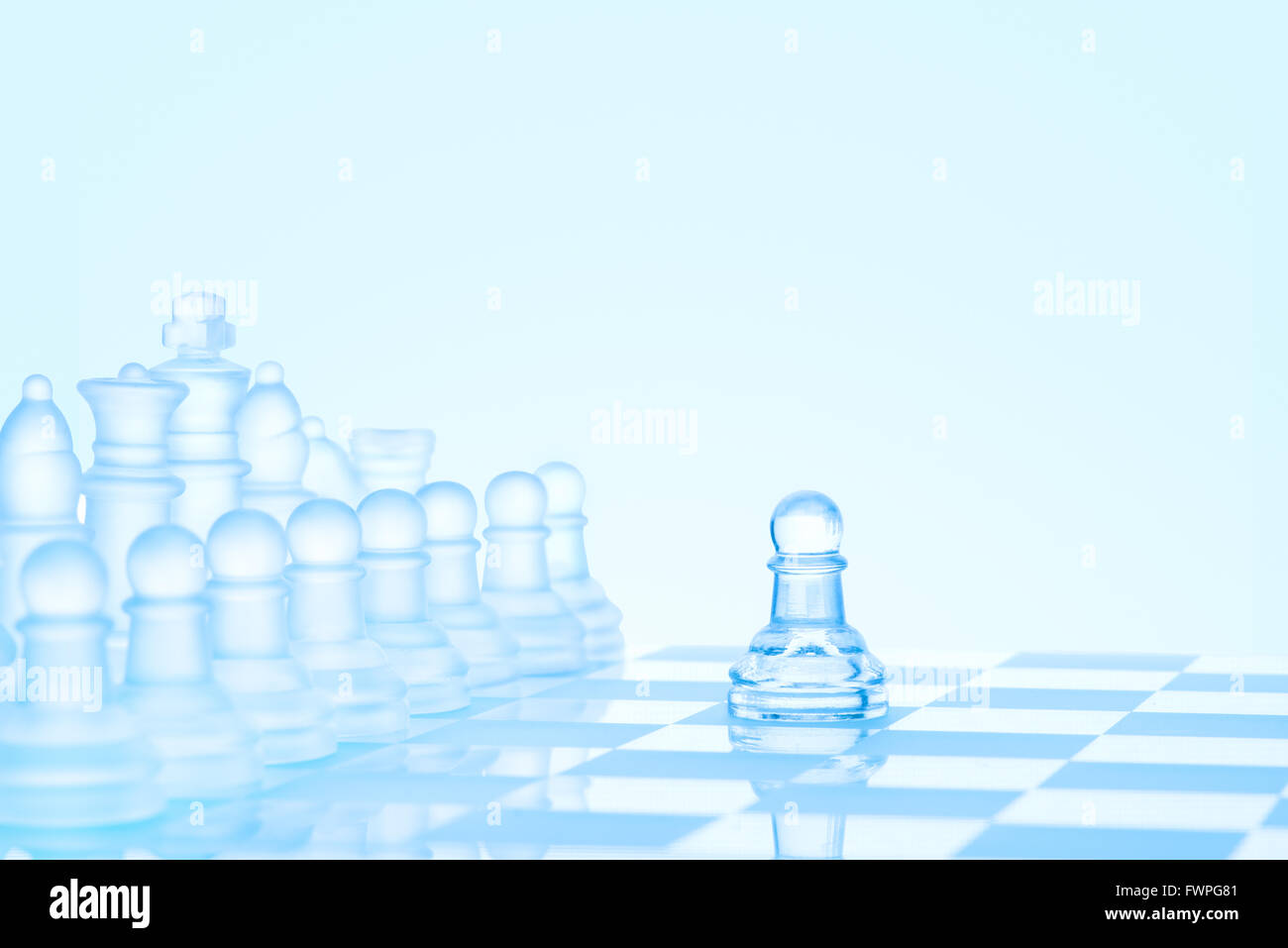 Leadership and bravery concept; an icy frosted single pawn staying against a full set of chess pieces on chessboard. Stock Photo