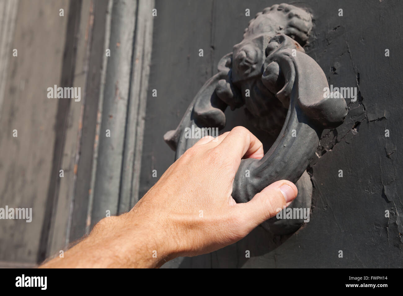 Male hand knocking old black door with metal ring knocker Stock Photo