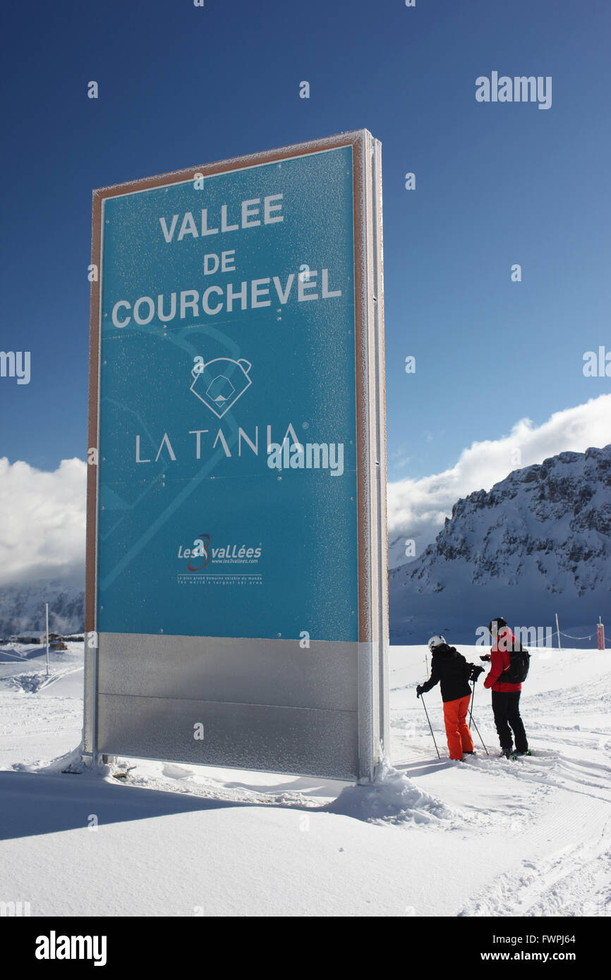 Two skiers on a sunny day next to a sign for the Vallee de Courchevel La Tania in the Three Valleys ski area in the French Alps Stock Photo
