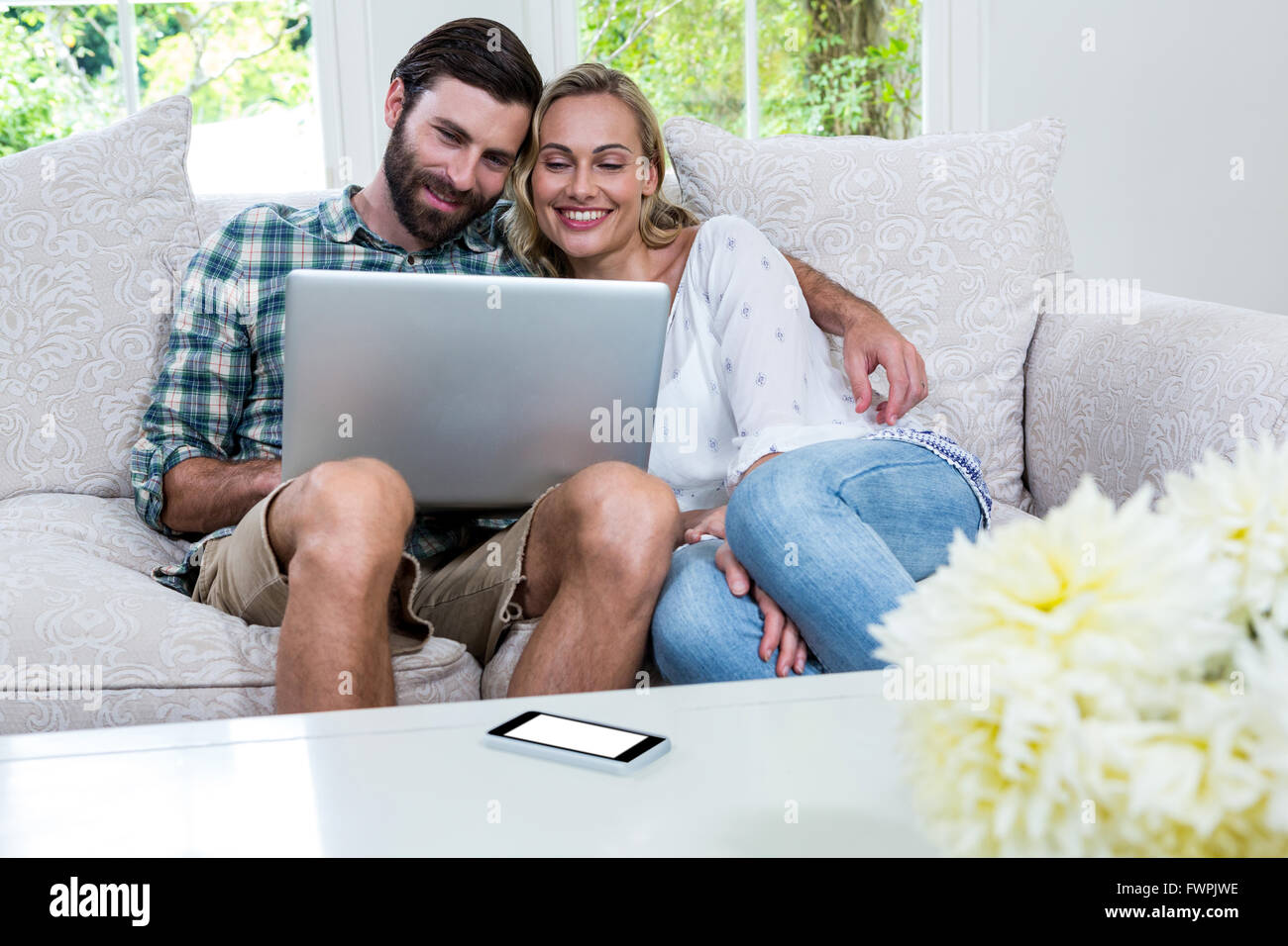 Happy young couple using laptop while sitting on sofa Stock Photo - Alamy